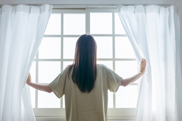 窓辺でカーテンを開けて、深呼吸している女性