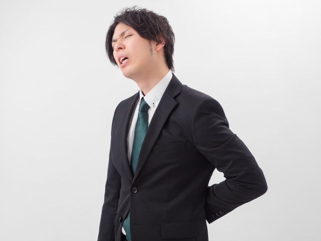 デスクで前かがみになり、腰に手を当てている会社員