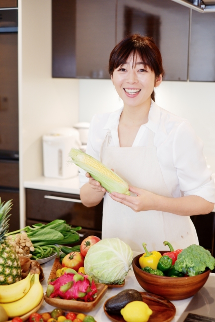 キッチンで野菜を手に、笑顔で食事を整えている女性