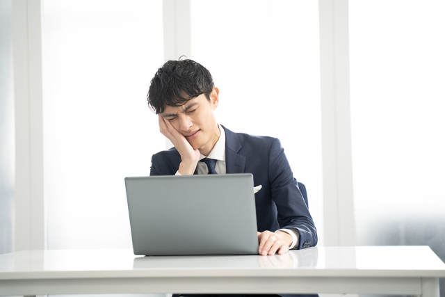 頬杖をついて疲れた表情でパソコンに向かう会社員