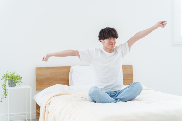 ベッドの上で、朝に腕を伸ばしてストレッチをする男性