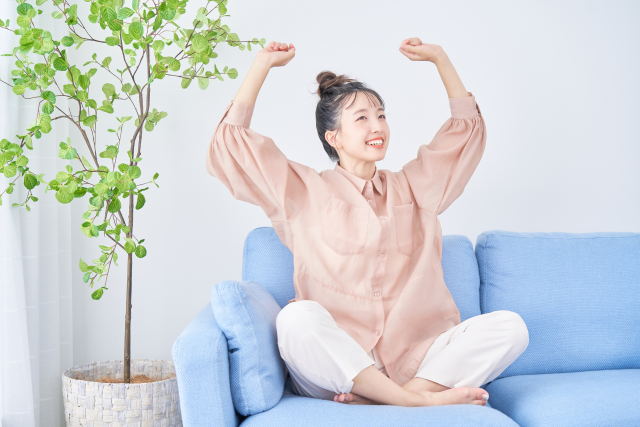 ソファの上で両腕を上げて、気持ちよさそうに伸びをする女性