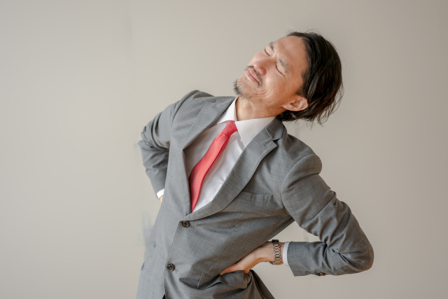 デスクで前かがみになり、腰に手を当てているビジネスパーソン