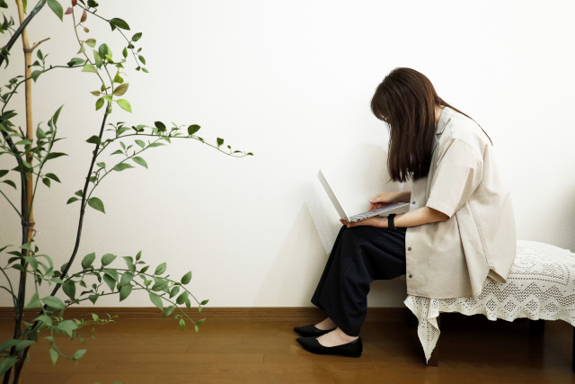 ベンチでノートパソコンを使い、背中を丸めている女性