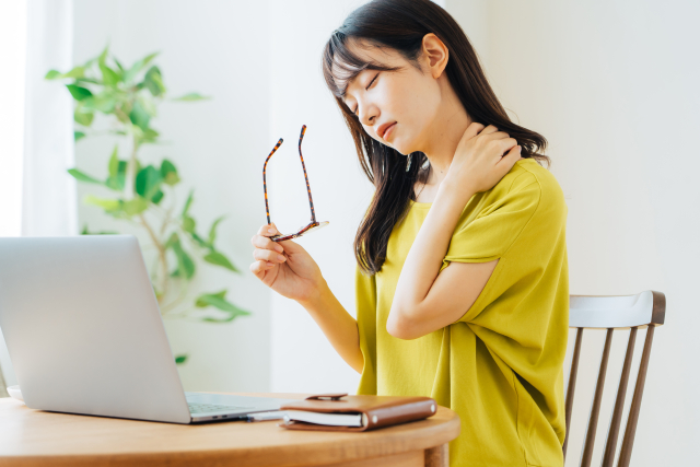 パソコン作業中に、首や肩に手を当てている女性