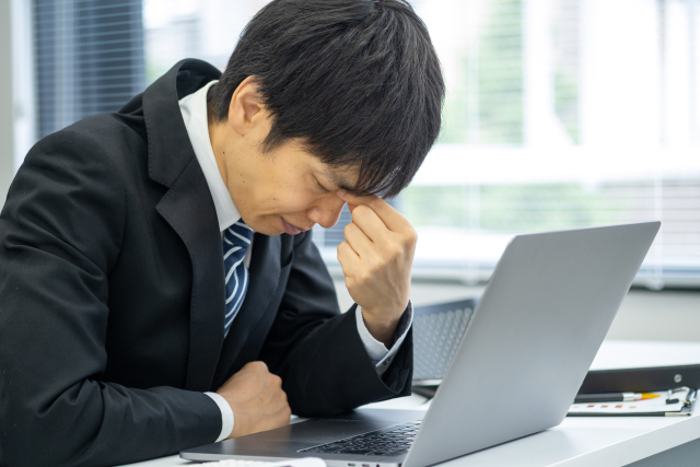 デスクで頭を抱えて、疲れた表情の会社員