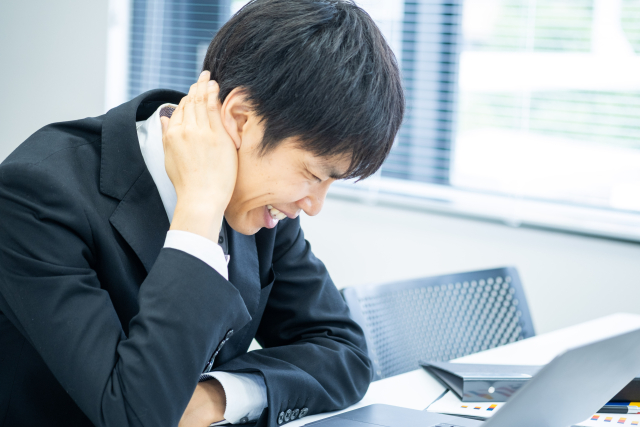 デスクで首に手を当てて、つらそうなビジネスパーソン
