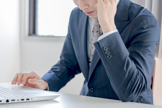 背中を丸めて、長時間パソコンに向かっている会社員