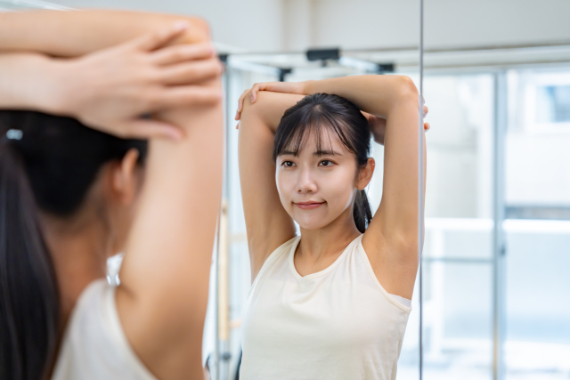 鏡の前で、姿勢を確認しながら腕を上にのばしている女性