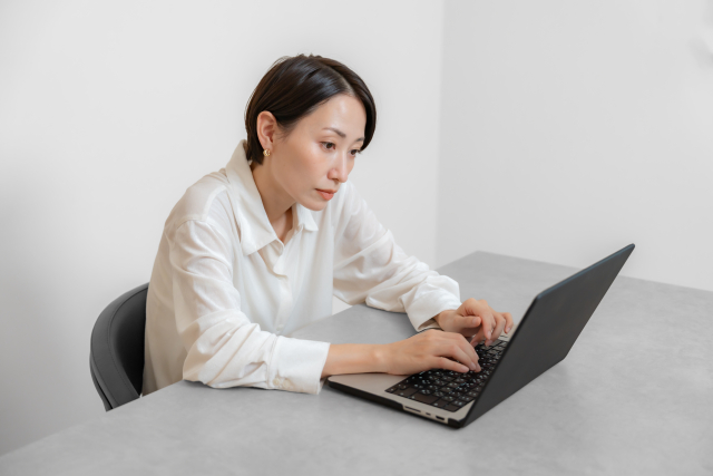 背中を丸めて、デスクでパソコン作業をしている女性